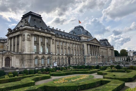 The Royal Palace in Brussels, Belgium, displays classical architecture and a landscaped garden under a partly cloudy sky.