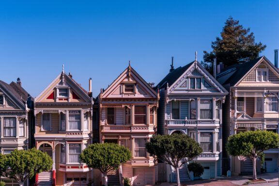 A row of colorful Victorian houses in San Francisco under a clear blue sky.