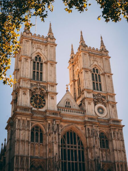 A sunlit image of Westminster Abbey's Gothic architecture, framed by tree branches.