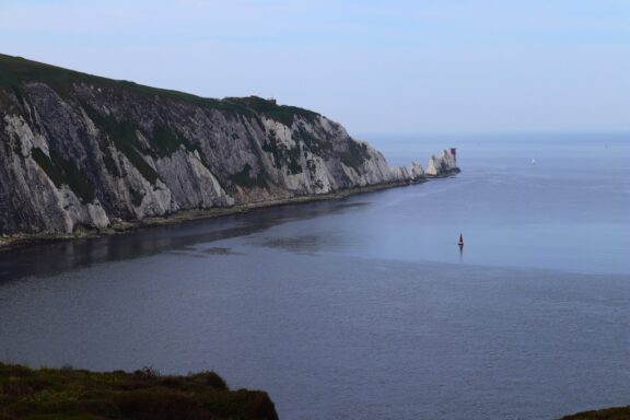 A serene view of a coastline with chalk cliffs and calm blue waters under a hazy sky.