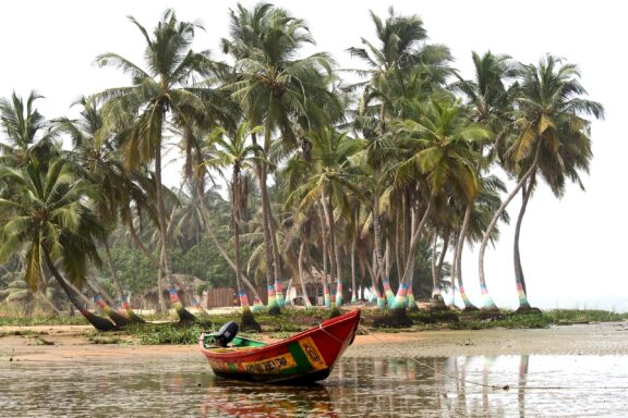 A colorful boat on the shore with a backdrop of palm trees, located in Ada, Ghana.