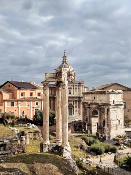 An image of the Arch of Severus at the Roman Forum, featuring ancient Roman ruins with columns and arches under a cloudy sky.