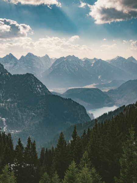 A picturesque view of the Bavarian Alps in Germany, featuring mountain layers, a misty valley, and dense evergreens.