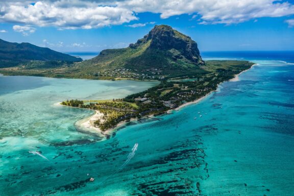 Aerial shot of Beachcomber Resort, Mauritius, featuring turquoise waters, sandy coast, greenery, and a mountain backdrop.