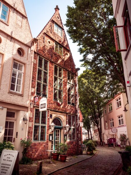 A narrow cobblestone street in Bremen with traditional German brick buildings, one prominently in the foreground, and a clear sky.