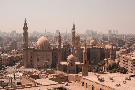 Aerial view of Cairo, Egypt, showcasing the dense urban landscape with historic mosques and minarets under a hazy sky.