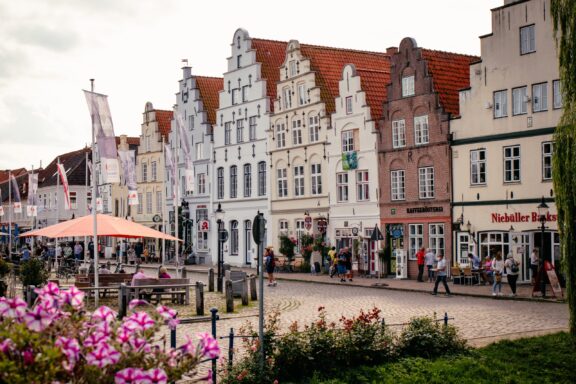 A German street view with traditional buildings, pedestrians, a café, and flowers adding a natural touch to the urban scene.