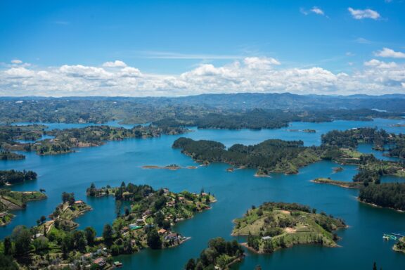 Aerial view of Colombia's Guatapé Reservoir displays small islands and peninsulas with lush greenery amidst blue waters.