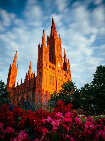 Twilight View of the Marktkirche with Illuminated Facade in Wiesbaden, Germany Marktkirche in Wiesbaden, Germany, with a vibrant red and blue sky backdrop and foreground of red flowers.