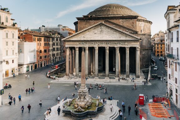 A scene at the Pantheon in Rome, featuring large columns, a fountain, and bustling crowd.