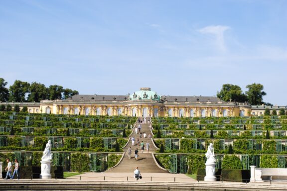 A photo shows Park Sanssouci's grand terraced vineyard and historic palace under a clear blue sky in Potsdam, Germany.