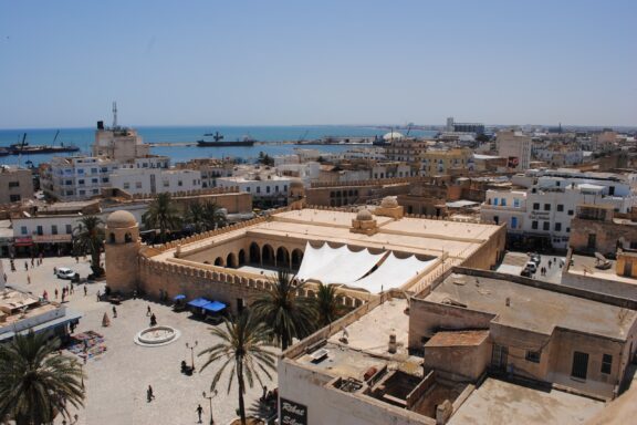 Aerial view of the coastal city of Sousse in Tunisia, showcasing the Mediterranean Sea, buildings with traditional architecture, and a clear sky.