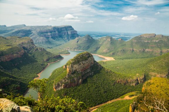 A picturesque view of a winding river in a green canyon with layered rocks under a semi-cloudy sky, possibly in South Africa.