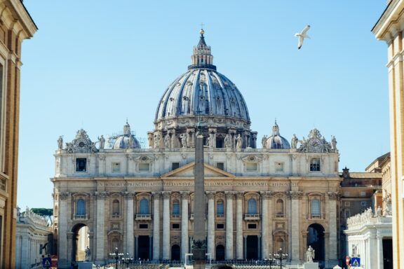 A photo of St. Peter's Basilica in Vatican City, showcasing the front facade and dome under a clear blue sky.