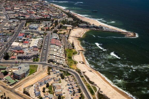 Aerial view of Swakopmund in Namibia, showcasing the coastal town with buildings adjacent to the beach and waves crashing onto the shore.