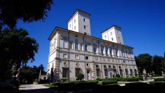 The Borghese Gallery in Rome is a three-story Renaissance building with white façades, symmetrical windows, and green surroundings.