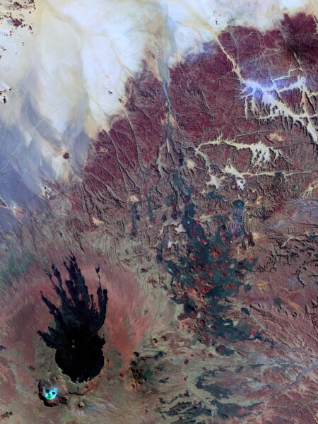 Aerial view of the Tibesti Mountains in Chad, featuring rugged terrain with various shades of brown and red, and a prominent dark volcanic crater.