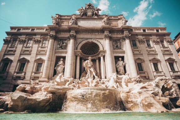 An image of the Trevi Fountain in Rome, showing its intricate sculptures and cascading water under a clear sky.