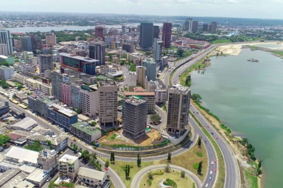 Aerial view of Abidjan cityscape with tall buildings, roads, and a water body in Ivory Coast.