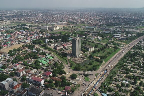 Aerial view of Kinshasa, Congo, showcasing dense urban development with buildings, roads, and greenery under a hazy sky.