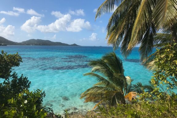 A tropical view of clear turquoise waters at Cayo Cangrejo, Providencia, framed by green foliage and distant hills.