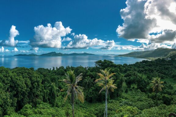 A scenic panorama of Chuuk, Micronesia's green landscape, palm trees, calm sea, and partly cloudy sky.