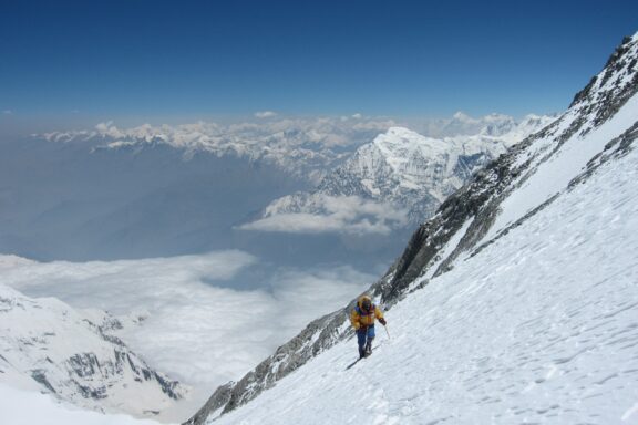 A climber ascending a snowy slope with the panoramic view of the Dhaulagiri mountain range in the background.