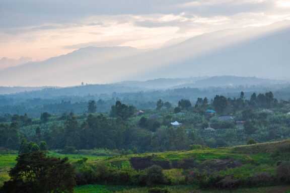 A scenic view of the lush green landscape near Fort Portal, Uganda, with rolling hills and a hazy sky at dusk.