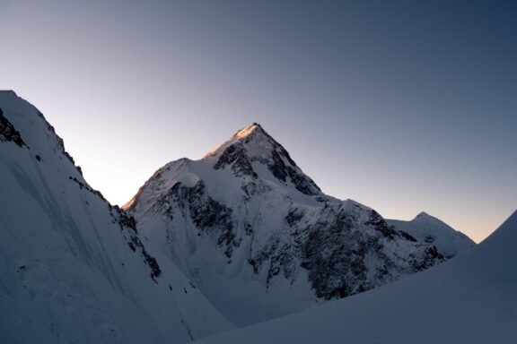 A twilight photo of Gasherbrum I mountain in the Karakoram range, with the sunset casting a warm glow on its snowy peak.