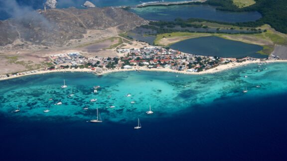 Aerial view of Gran Roque, Venezuela displays a coastal village, beach with boats, and clear turquoise waters.