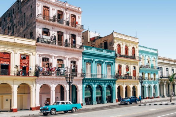 A vibrant Havana street scene with pastel-colored buildings and a classic blue car parked upfront.