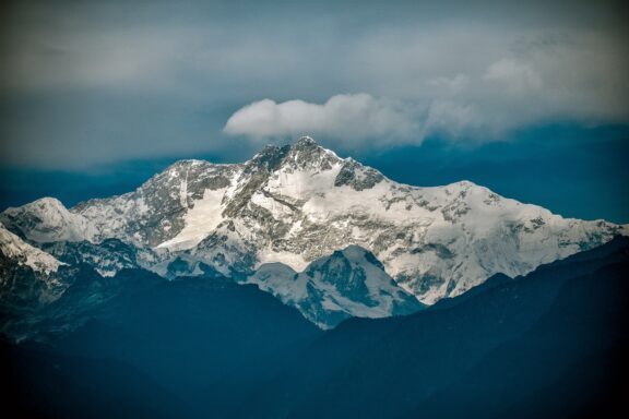 A view of Kangchenjunga mountain with snow-covered peaks under a cloudy sky.