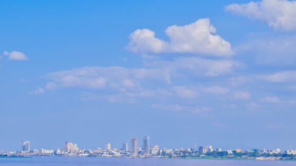 A panoramic view of Kinshasa's skyline under a blue sky with scattered clouds.