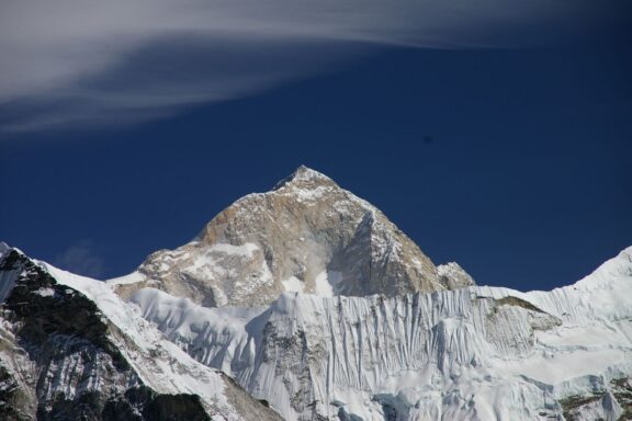 A snow-capped mountain peak under a blue sky with wispy clouds, likely Mount Makalu.