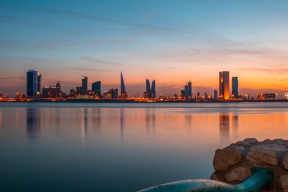 Sunset view of Manama skyline with reflections on water in Bahrain.