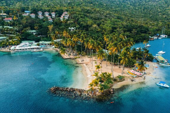 Aerial view of Marigot Bay in Saint Lucia, showcasing the clear blue waters, sandy beach, lush greenery, and boats docked along the shore.