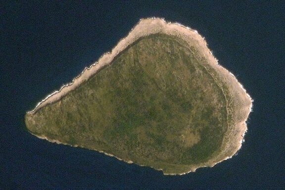 Aerial view of Navassa Island, showing a small, triangular-shaped island with rocky shores and dense green vegetation in the center.