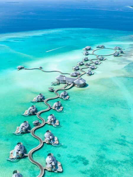 Aerial view of overwater bungalows with curving walkways in Noonu Atoll, Maldives, surrounded by turquoise waters.