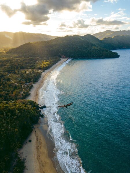 Sunset aerial view of Playa el Valle beach in the Dominican Republic, with sunlight illuminating the shoreline and greenery.