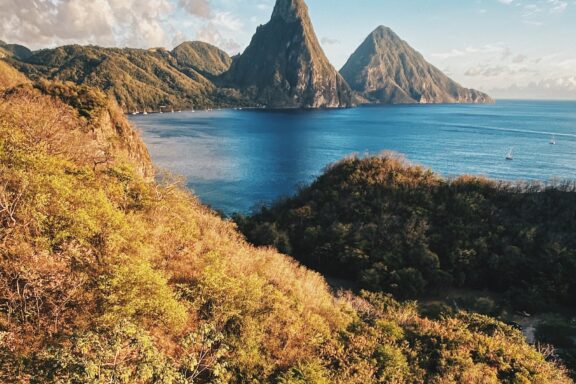 A scenic view of the Pitons in Saint Lucia, with lush greenery in the foreground and clear blue skies above.