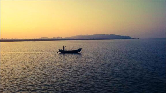 A lone boat with a person on calm waters at dusk or dawn with a silhouette of a landmass on the horizon, possibly in Saint Martin.