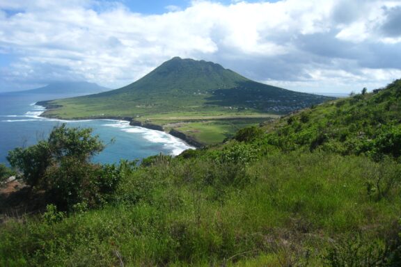 A picturesque view of a green landscape, mountain, coastal waters, and clear sky, likely in Sint Eustatius.