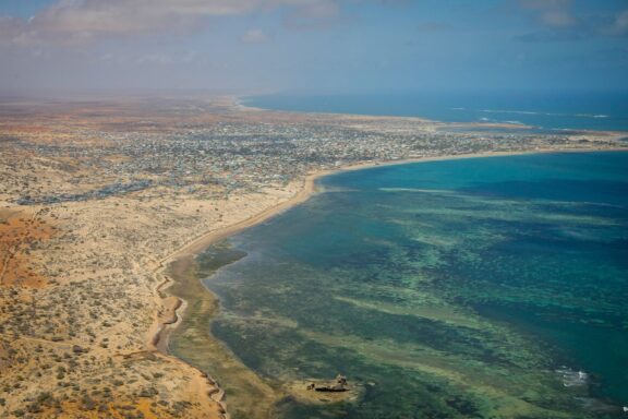 Aerial view of Somalia's semi-arid coast, sparse vegetation, clear blue sea, and a coastal settlement.