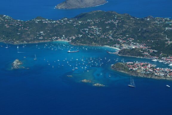 Aerial view of a coastal area in St. Kitts and Nevis with boats scattered in the blue waters near the shoreline, surrounded by lush greenery.