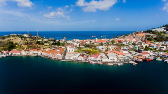 Aerial view of The Carenage in Grenada, showing colorful buildings along the waterfront with boats docked in the harbor and hills in the background.