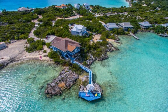 Aerial view of coastal properties on the Turks and Caicos Islands with clear turquoise waters and scattered vegetation.