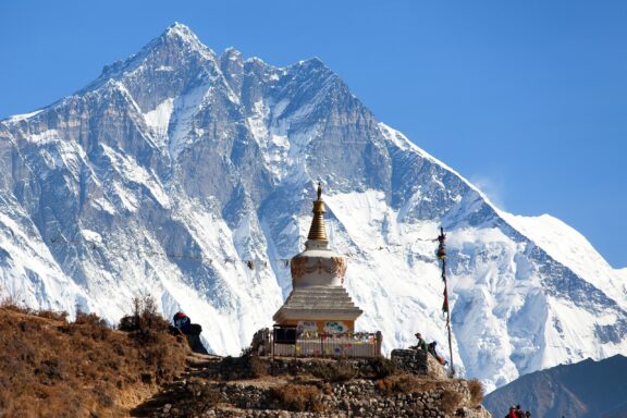 A Buddhist stupa in the foreground with Mount Lhotse, the fourth highest mountain in the world, in the background under a clear blue sky.