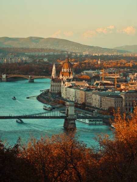 A sunset view of Budapest with the Danube River, a bridge, the Parliament Building and hills.