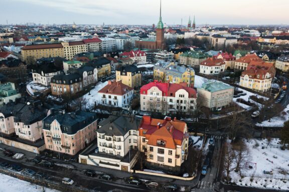 Aerial view of Helsinki's Eira neighborhood showcases historic buildings, snow-covered streets, bare trees, and a distant church spire.