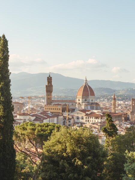 A scenic view of Florence, Italy, with the iconic Duomo and bell tower in the foreground and rolling hills in the background, under a soft sky.